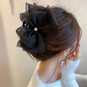 Detail view of a black mesh bow hair claw with a crystal center worn on a bun hairstyle