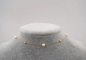 Detail of freshwater pearl necklace with gold-plated beads on a grey display bust