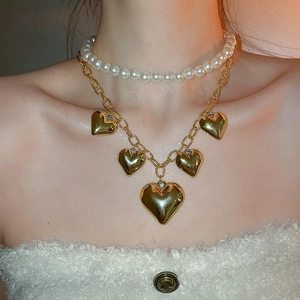 Close-up of layered necklace featuring white pearls and golden heart charms on chain