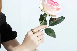 Détail d'une bague dorée en cœur sertie de cristaux sur fond de roses roses