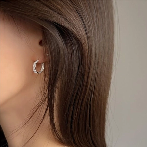 Close-up of sparkling silver C-shaped hoop earrings with zircons on model ear