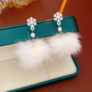 Close-up of snowflake earrings with pearl and white pompom on a jewelry box edge