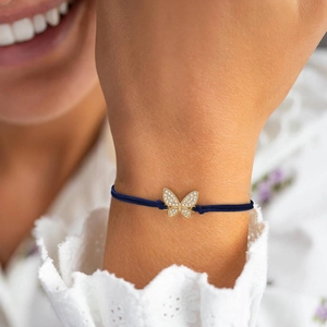 Detail of 18K gold butterfly charm with clear diamonds on a navy blue woven rope bracelet