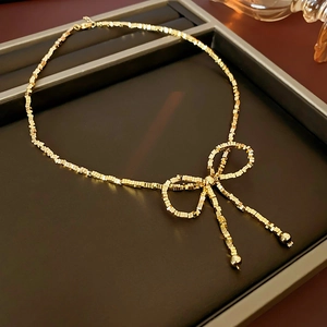 Close-up of golden bow-tie pendant with minimalist square bead chain and adjustable clasp