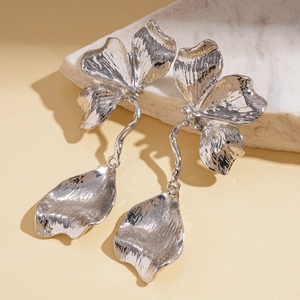 Detailed macro view of silver metallic flower earrings with textured petals on marble