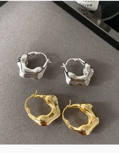 Détail de boucles d'oreilles créoles ondulées en métal doré et argenté poli