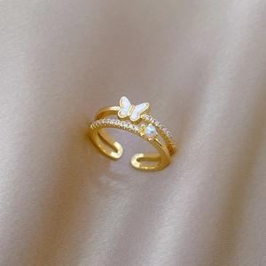 Détail d'une bague papillon dorée ajustable avec perles sur fond en satin