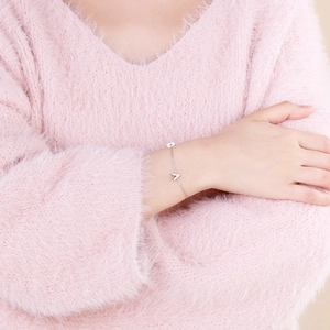Close-up of a silver V-shaped pendant bracelet worn on a pink knitted sweater sleeve