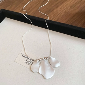 Close-up of matte silver petal pendants on a sleek snake chain against beige canvas