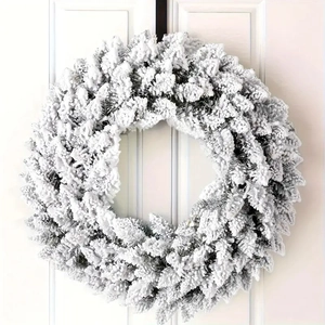 Winter cedar Christmas wreath with white flocking hung on a minimalist white door