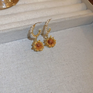 Macro view of sunflower earrings with C-shaped pearl hoops and golden metal petals
