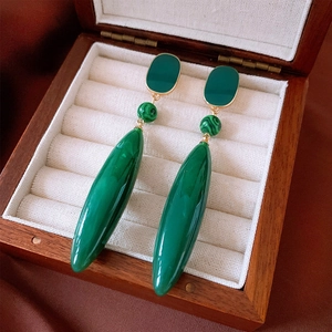 Detail of vintage emerald green teardrop earrings with gold plating on velvet cushion
