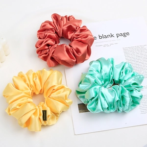 Close-up of satin scrunchies in orange yellow and green with elegant pleated texture