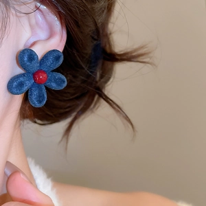 Detail of blue flocked flower earring with a red bead center on model's ear