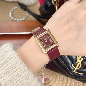 Close-up of a rectangular gold watch with red dial and leather strap on a wrist