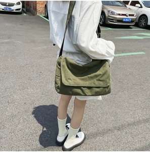Detailed view of an army green canvas crossbody bag worn by a model in a casual street setting