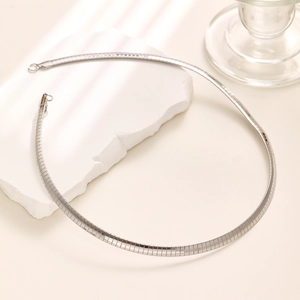 Polished silver flat snake chain necklace on a textured white stone platform pedestal