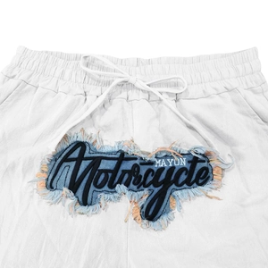 Detail einer weißen Hose mit Denim-Patchwork, Motorrad-Stickerei und ausgefransten Kanten