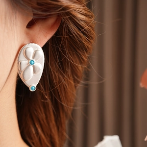 Detail of silver drop earring with floral relief and turquoise beads worn by a model