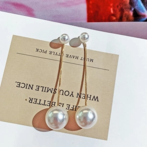 Detail of long drop earrings featuring white faux pearls and gold-tone snake chains