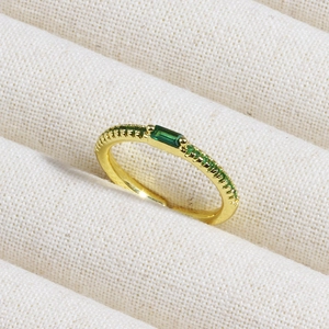 Detailed macro view of golden ring with emerald stones on soft beige knit fabric