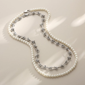 Détail montrant le collier de perles blanches superposé et la chaîne en acier nouée