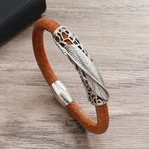 Macro shot of brown braided leather bracelet with silver feather metal charm and magnetic clasp