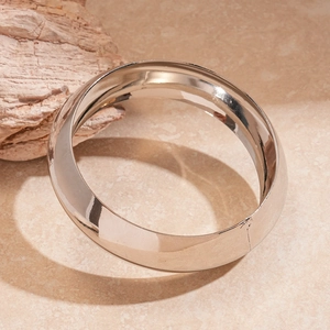 Macro view of polished silver Mobius twist metal bangles on a textured beige surface