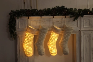 Detail of four white knitted Christmas stockings with fish scale pattern on fireplace