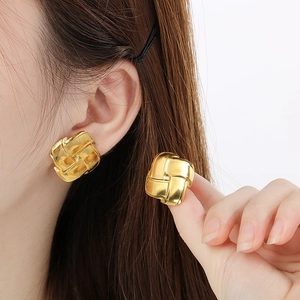 Macro shot of gold square earrings with vintage woven texture held in hand