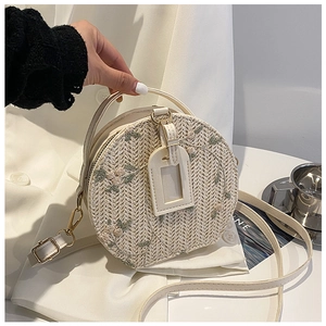 Detail of round beige straw bag featuring delicate floral embroidery and leather handles