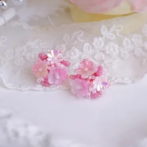 Close-up of handmade pink beaded flower earrings on white lace background fabric