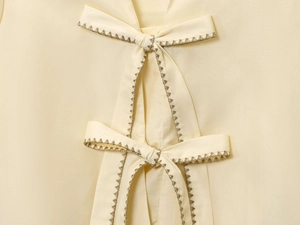 Detailed view of beige striped poplin shirt featuring bow ties and decorative stitching