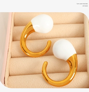 Macro shot of gold C-shaped earrings with white enamel studs in a jewelry display box