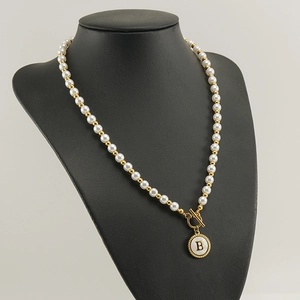 Detail of 18K gold OT buckle necklace with white pearl beads and round letter B pendant