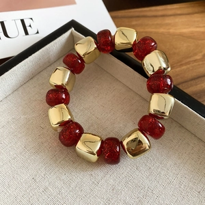 Detail shot of gold metallic square beads and translucent red resin beads on elastic bracelet