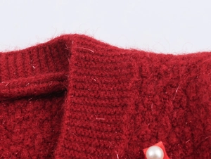 Dettaglio ravvicinato del cardigan rosso in maglia con filo dorato e bottone di perla bianca