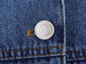 Close-up of denim jacket showing silver buttons and orange contrast stitching detail