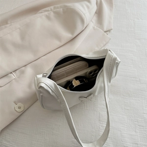 Minimalist white pleated underarm bag showing interior capacity with phone and wallet