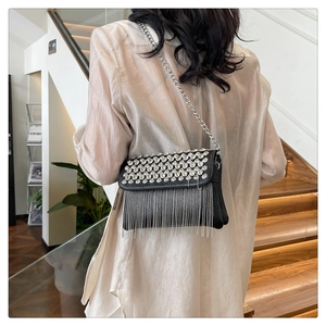 Detail of a black crossbody bag with shimmering rhinestone fringes and silver chain strap