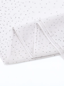 Close-up of sparkling rhinestones on elegant light-colored chiffon evening shawl fabric