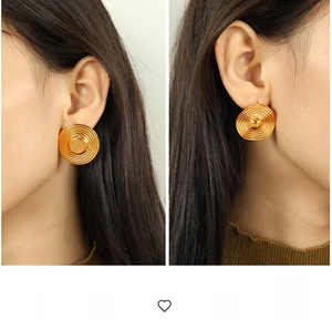 Close-up of golden concentric circle stud earrings with spiral textured relief on ears