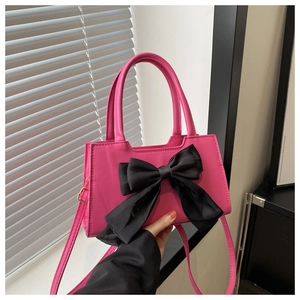 Detail of bright pink leather handbag with a large black bow and golden metal hardware