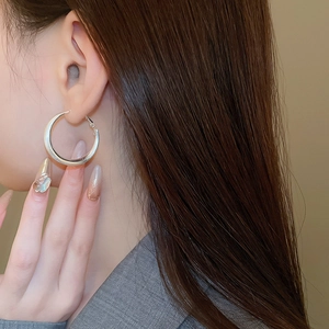 Detail of silver brushed crescent hoop earring worn by a model in a close-up shot