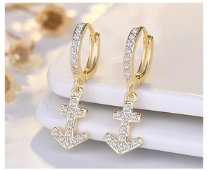 Macro shot of gold anchor earrings featuring sparkling white zircon on a white ceramic tray