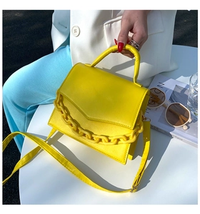 Detail of a bright yellow leather crossbody bag with a thick matching chain on a table