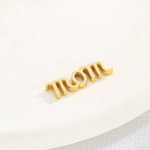 Pendentif MOM en acier inoxydable doré poli sur un plateau de présentation blanc