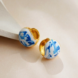 Macro detail of 18K gold hoop earrings with blue and white enamel splash pattern