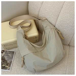 Borsa a tracolla in nylon beige presentata in un interno accogliente con valigia vintage