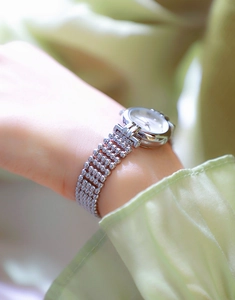 Close-up of a silver ladies' watch with a beaded metal strap on a silk-draped wrist